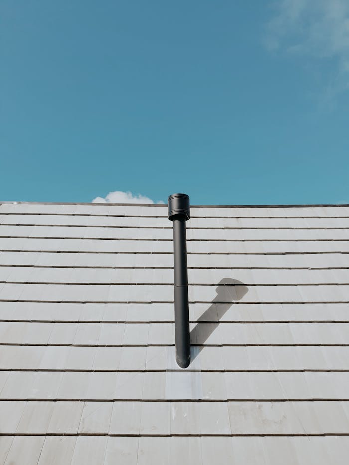 Slate roof with a black vent pipe under a clear blue sky. Minimalist architectural detail shot.